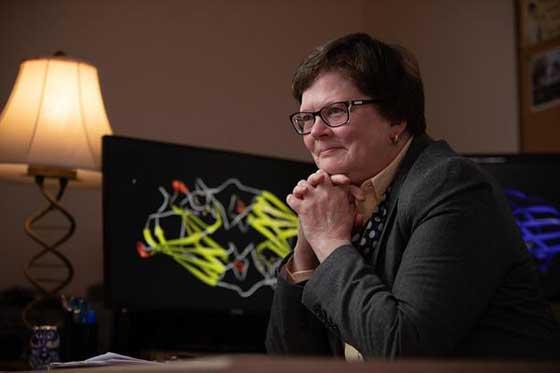 博士照片. 丽莎·兰伯特(Lisa Lambert)坐在桌子旁，身后放着一台电脑显示器和一盏灯