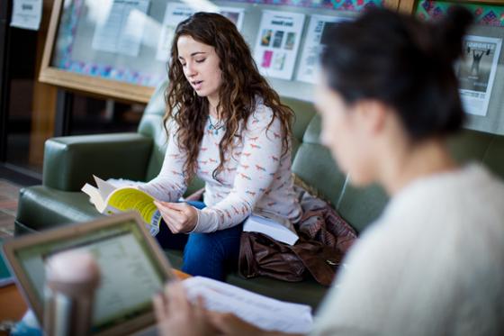 两名立博体育官网女学生在图书馆工作的照片, 一个在看书，一个在看电脑