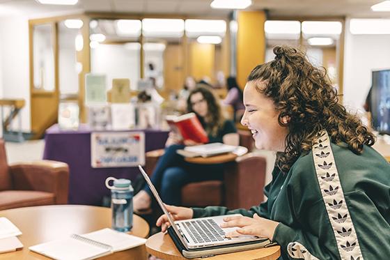图为一名立博体育官网的女学生在珍妮·梅隆·金图书馆的桌子旁工作时微笑的照片.