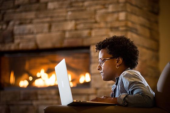 Photo of a Chatham University student working on her laptop in a leather chair in front of a fireplace in a student lounge