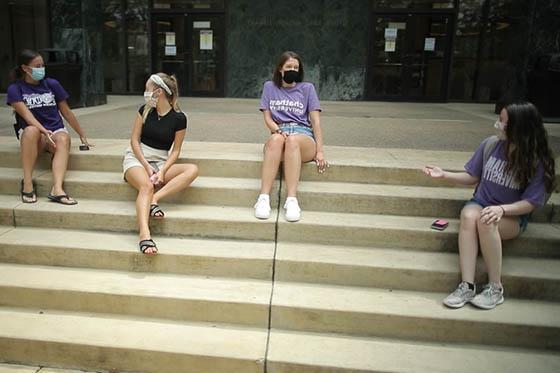 四名立博体育官网学生的照片，戴着面具，坐在图书馆的台阶上